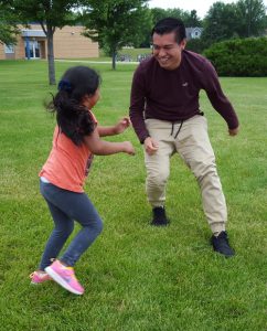 A young man and a little girl play tag in the grass.