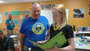 A woman stands reading from a binder to another man.