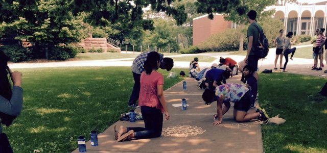 Kids draw on a sidewalk with chalk.