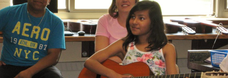 A girl sits playing guitar.